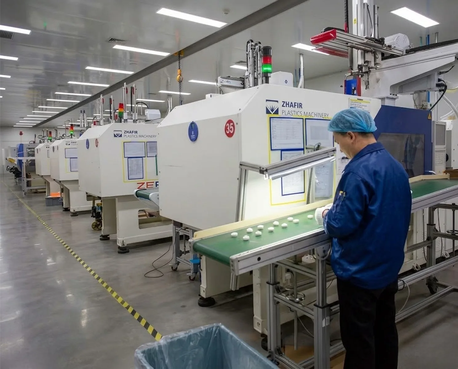 Worker in blue uniform operating automated injection molding machines to produce white cosmetic jars on a conveyor belt at LumLun factory