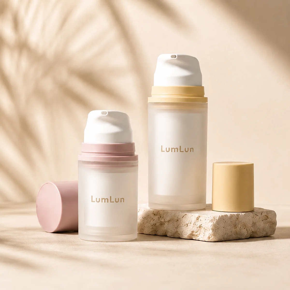 Two frosted PP airless pump bottles — small 30ml with pink collar and cap, larger 100ml with yellow collar and cap — displayed upright on a stone platform with detached caps beside them, soft palm leaf shadow background, LumLun OEM skincare packaging