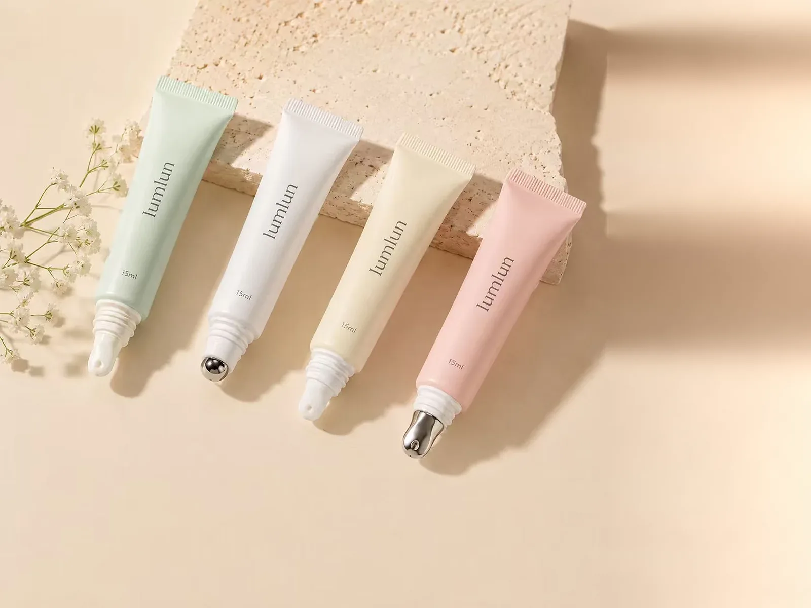 Four pastel LumLun 15ml cosmetic tubes with rollerball, nozzle, silicone and slanted metal applicator tips beside white baby's breath flowers