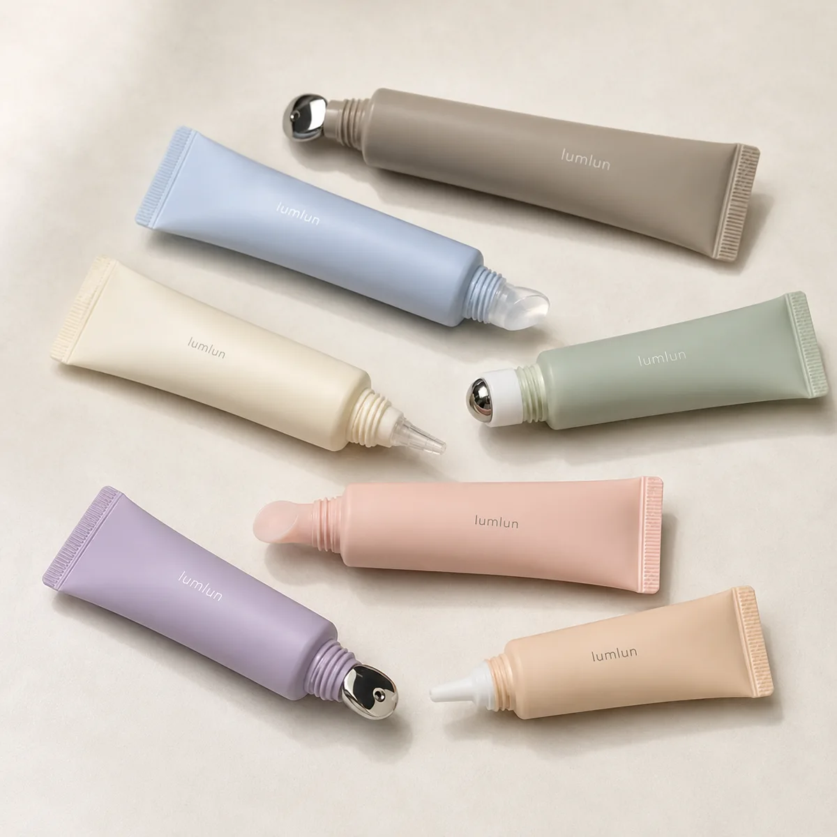 Seven pastel LumLun cosmetic squeeze tubes with different applicator tips: silver alloy massage scoops, clear silicone tips, fine nozzle tips and metal rollerballs