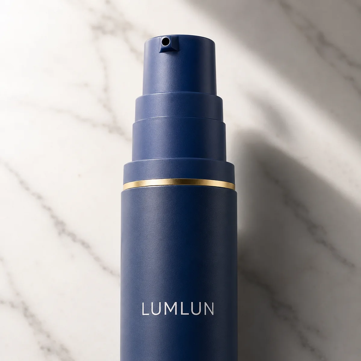 Close-up of a custom navy airless pump bottle with matte finish, gold decorative band, and printed logo for skincare branding