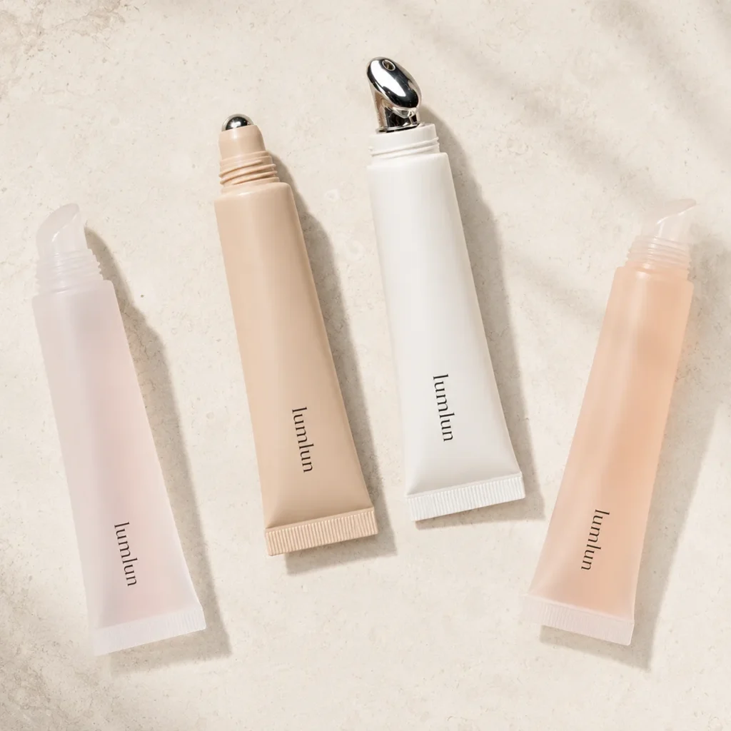 Flat lay of LumLun lip serum squeeze tubes with silicone, rollerball, and alloy massage applicator tips on a stone surface