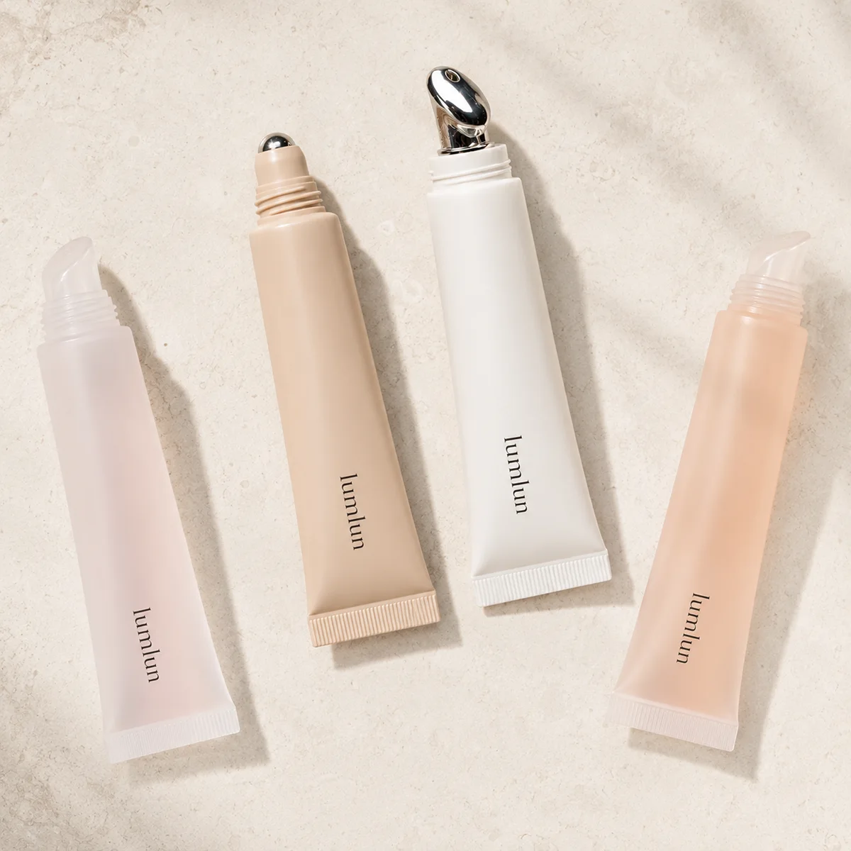 Flat lay of four LumLun lip serum applicator tubes with silicone, rollerball, and silver alloy massage tips in pink, beige, and white