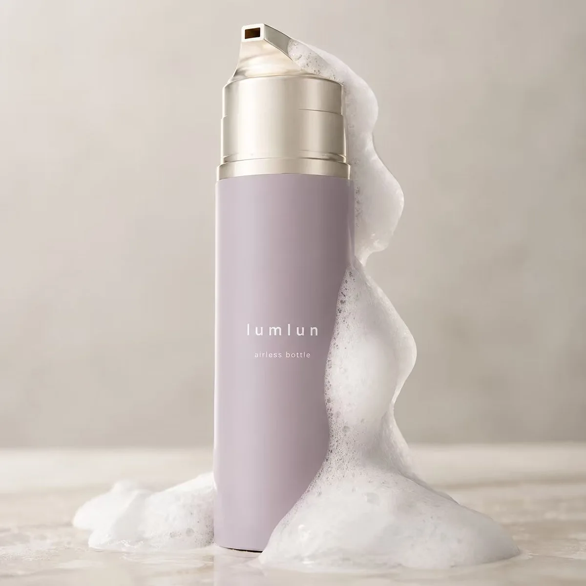 LumLun lilac airless foaming bottle with a gold pump top, dispensing foam down the side