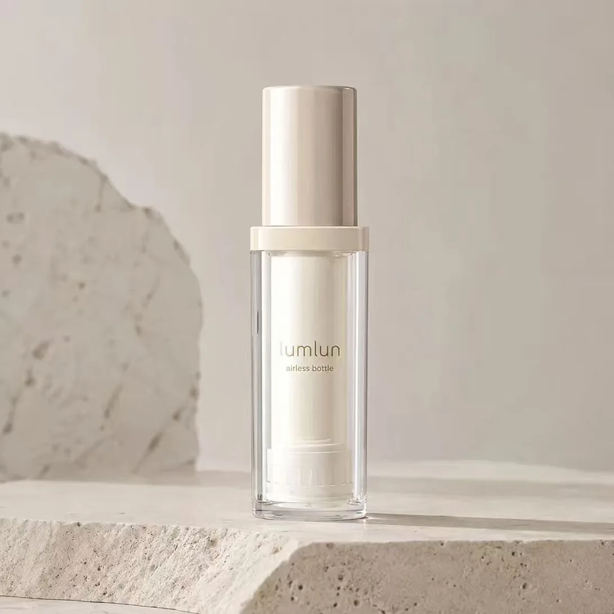 LumLun refillable airless bottle with a clear outer shell and cream cap, single bottle on a stone podium