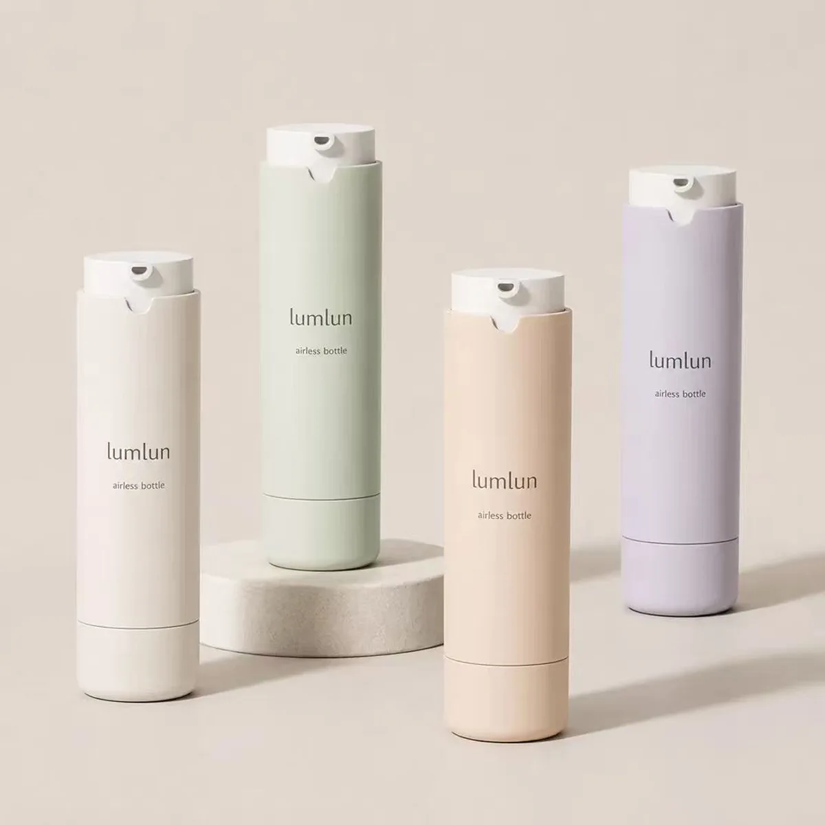 LumLun refillable airless pump bottles in cream, sage green, apricot and lilac on a stone podium