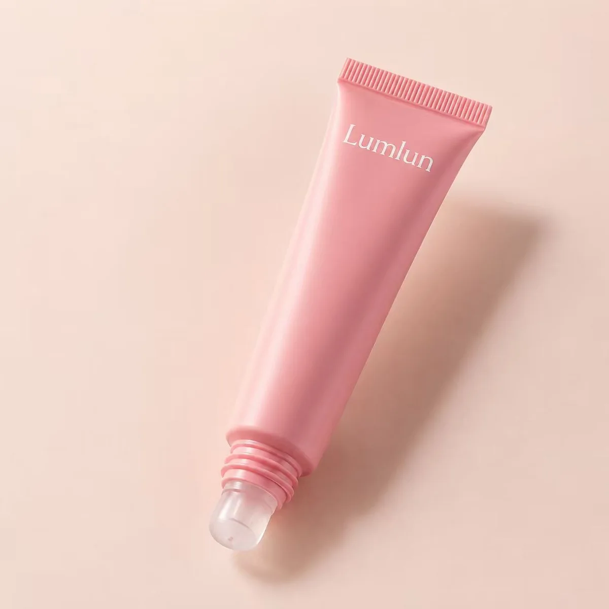 Pink LumLun squeeze tube with a soft clear non-porous silicone applicator tip for lip serums and oils on a blush background