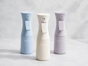 Three LumLun continuous mist spray bottles in pastel blue, ivory and lavender with ergonomic trigger designs