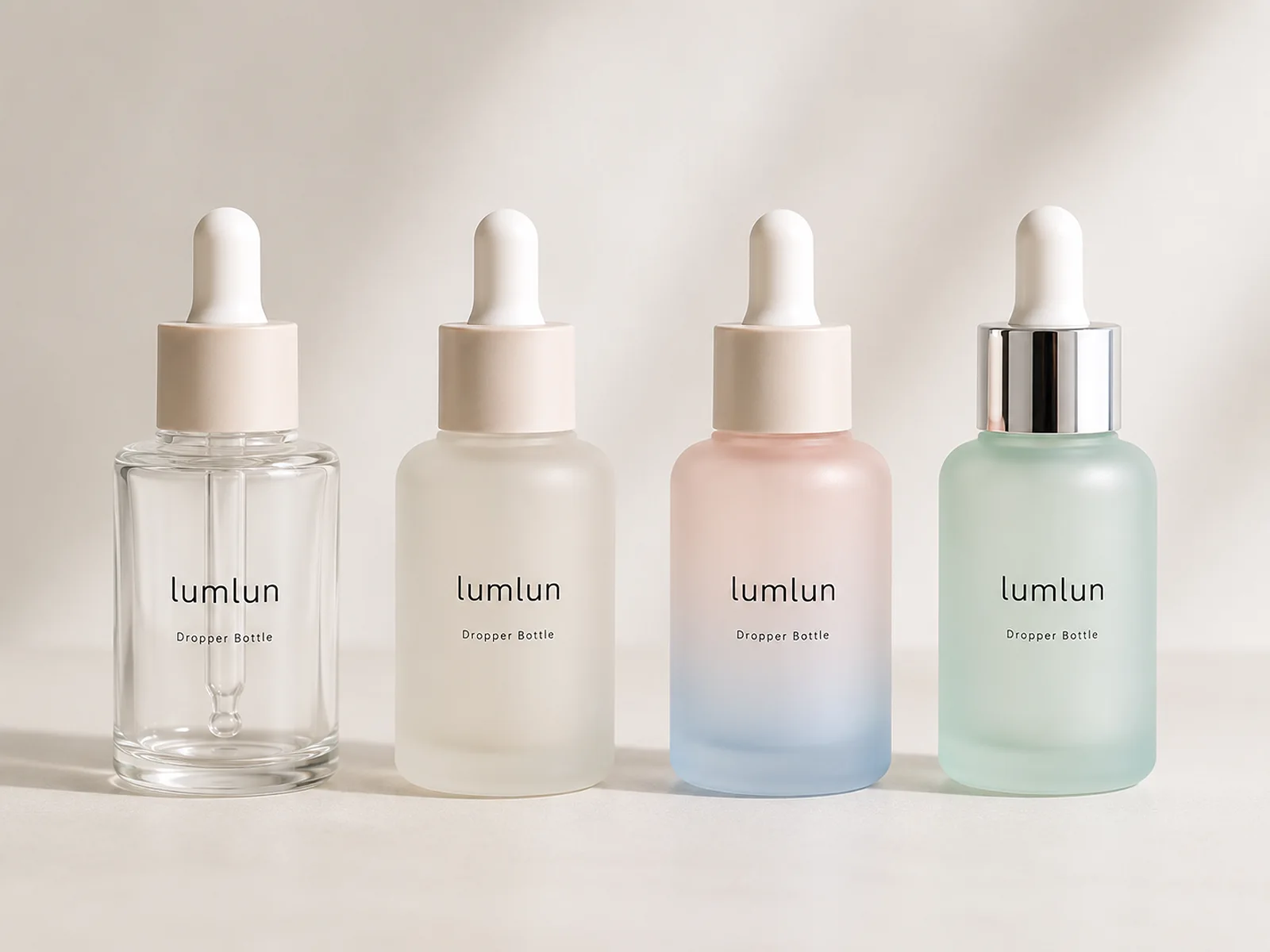 Four LumLun dropper bottles in clear, frosted ivory, pink-to-blue gradient and frosted mint finishes with cream and silver collars