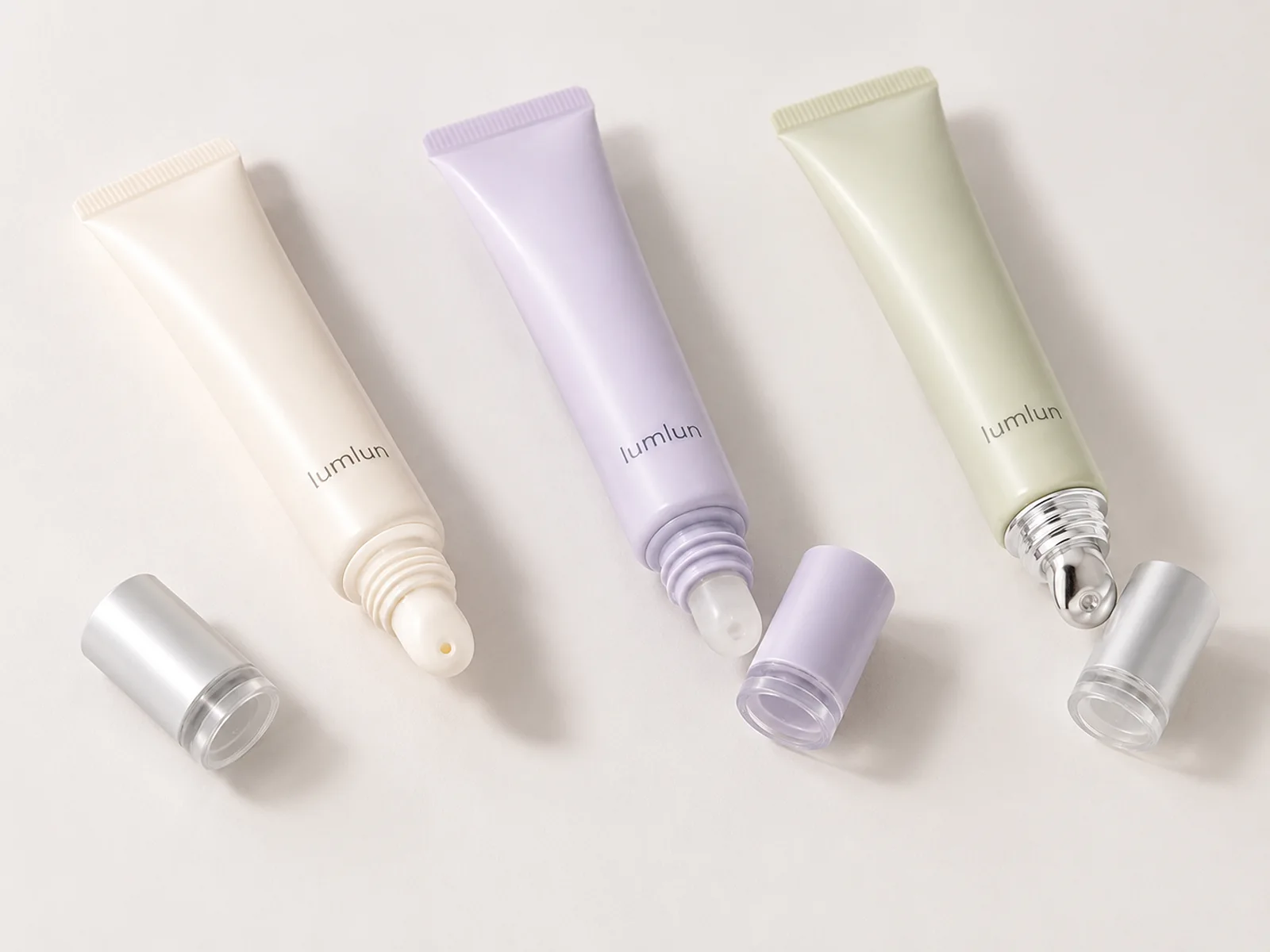 Three LumLun lip balm squeeze tubes in ivory, lavender and sage with rounded, clear and metal rollerball applicator tips
