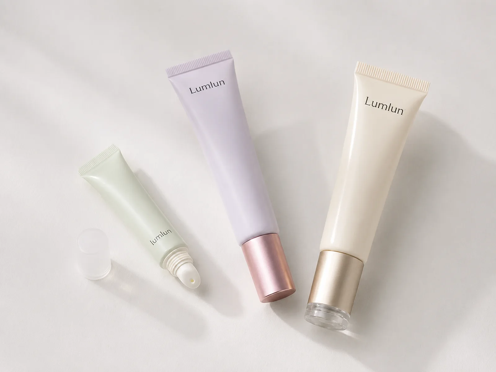 Three LumLun lip balm squeeze tubes in sage, lavender and ivory with different lengths, proportions and metallic-effect caps