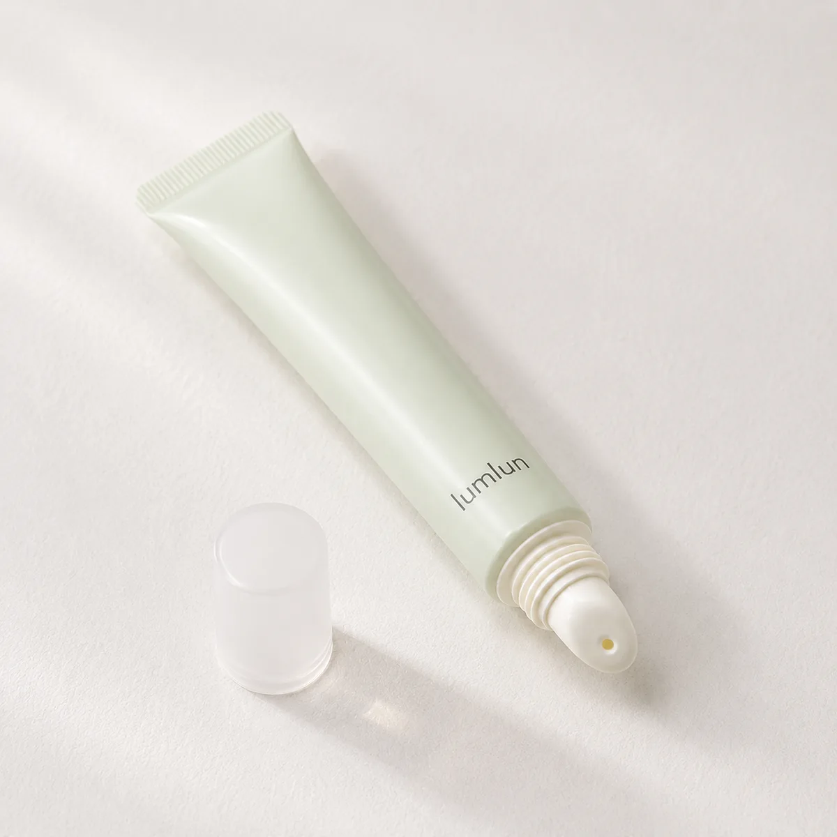 Single LumLun lip gloss squeeze tube in soft green color with cap placed beside it on a clean background.