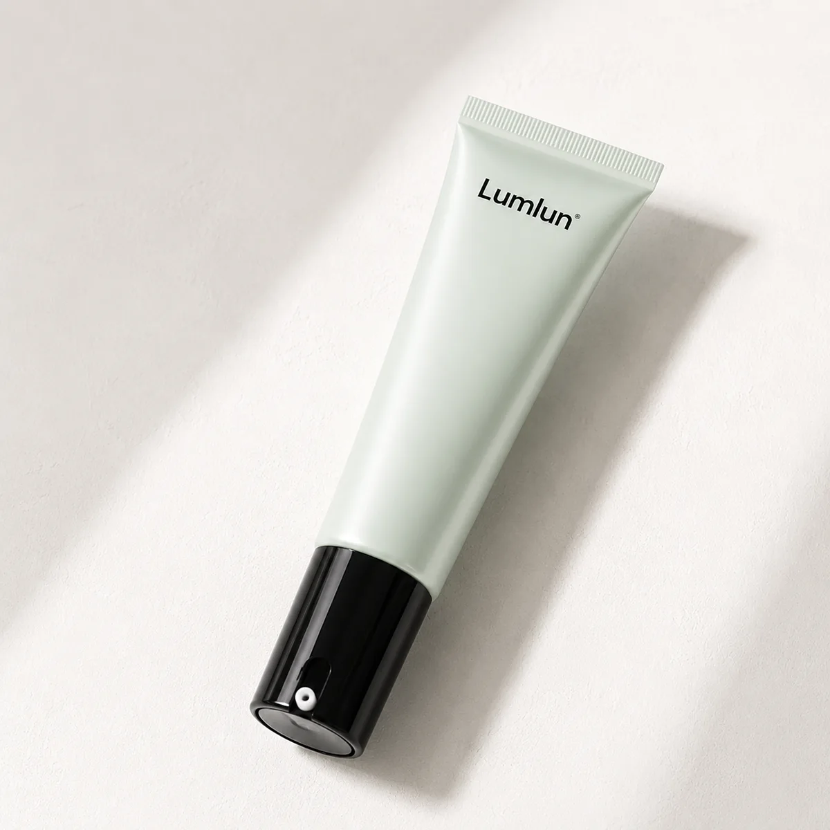A single LumLun airless squeeze tube in light green with black pump base shown in close-up studio lighting.