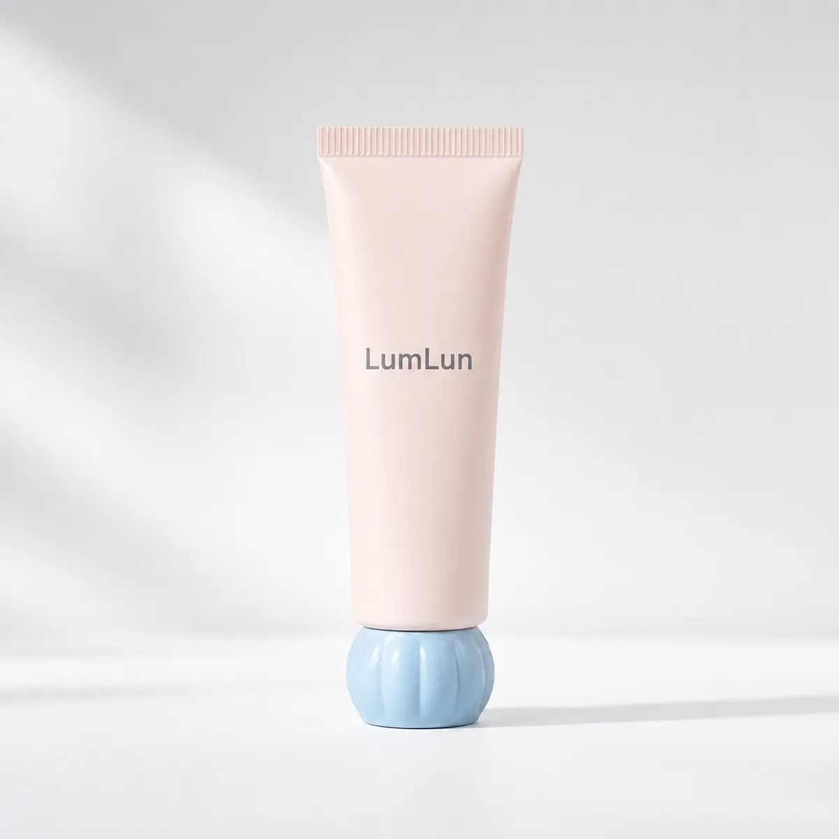 Single LumLun cosmetic squeeze tube in pink standing on a blue dome-shaped base in minimal studio lighting.