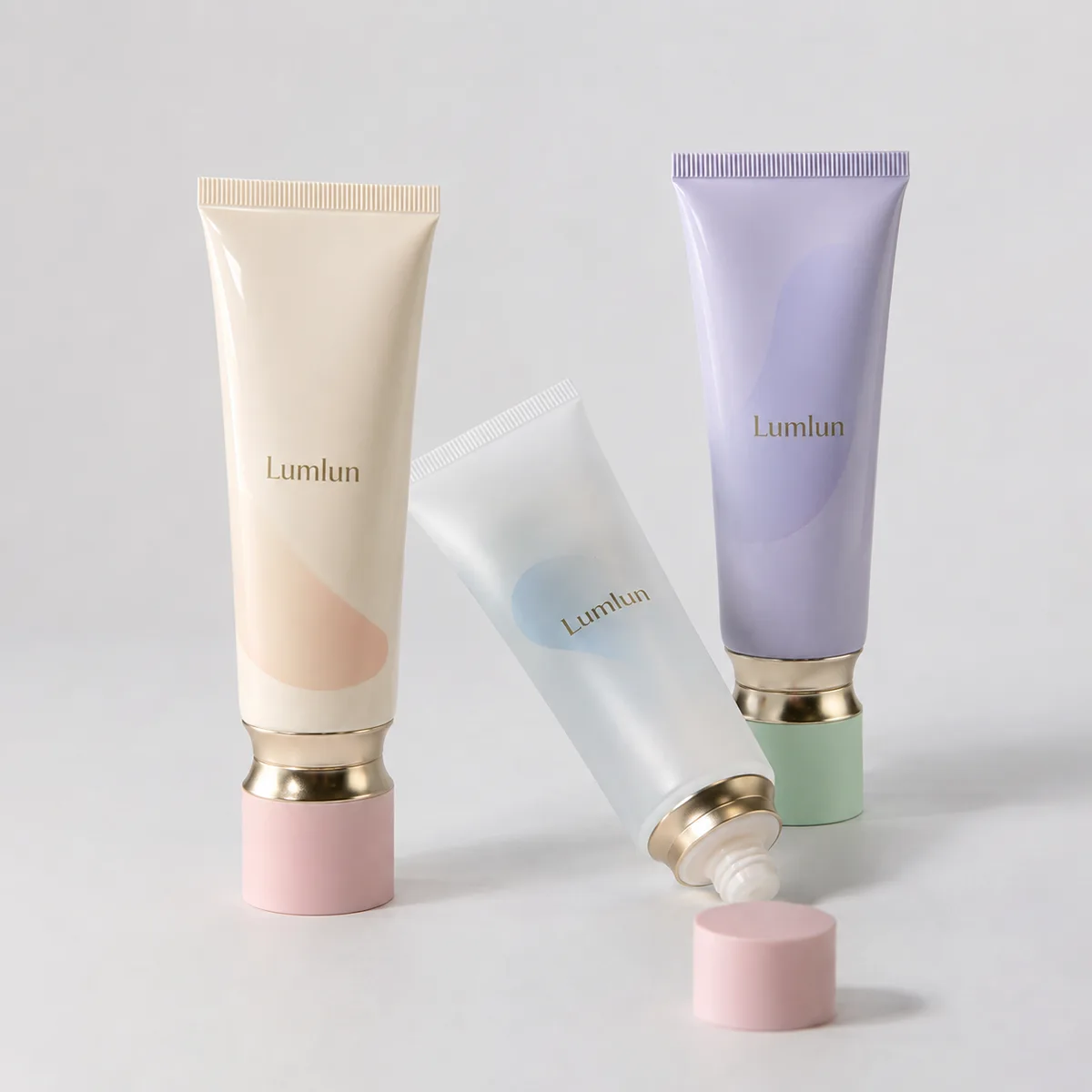 Three Lumlun cosmetic tubes with screw caps in cream, white, and lavender, including one open tube and a loose cap.