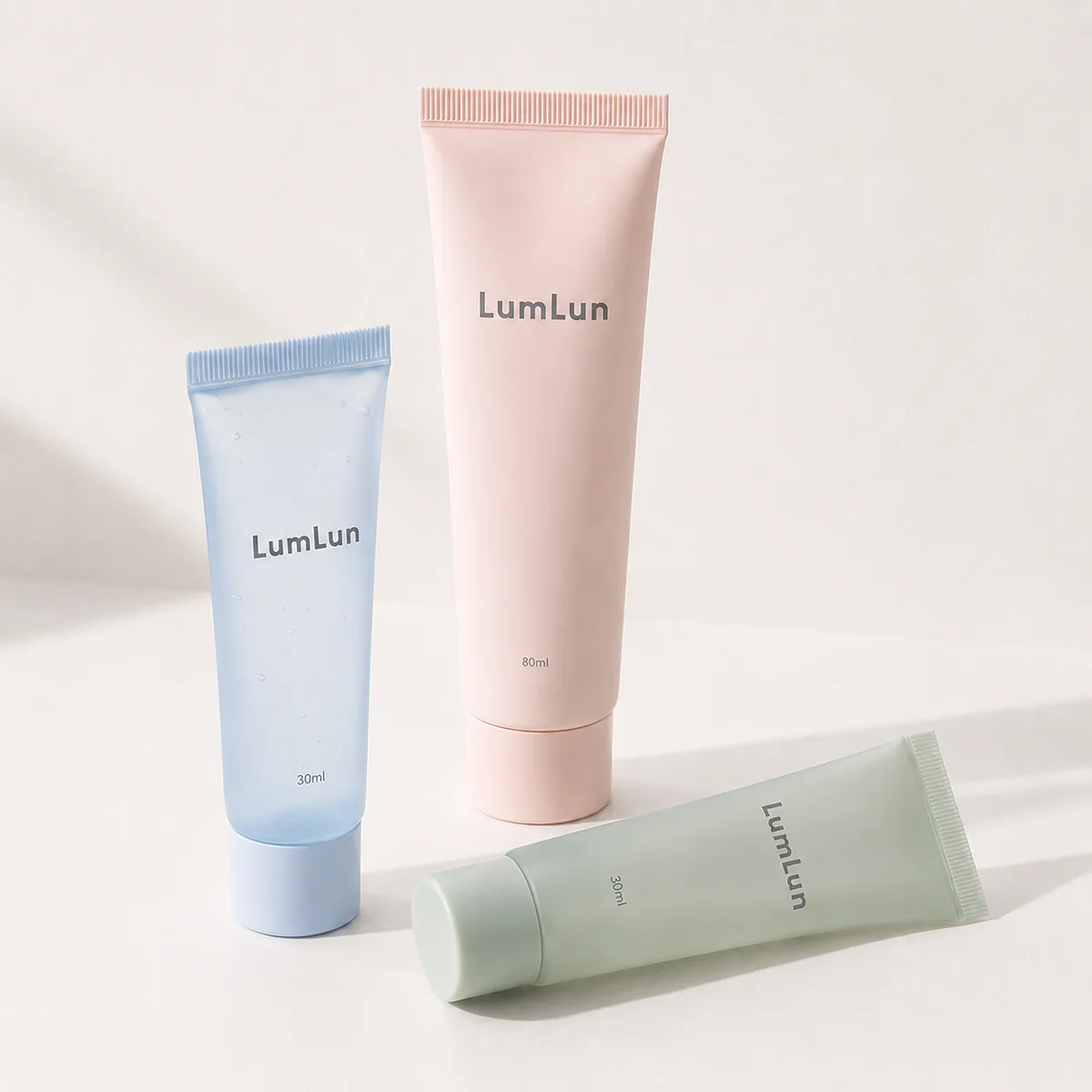 Three Lumlun cosmetic tubes in pastel blue pink and green, arranged with standing and lying positions in studio light