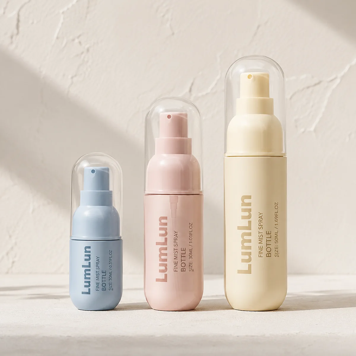 Lumlun fine mist spray bottles in blue, pink, and yellow with clear protective dome caps arranged in a minimal studio setting
