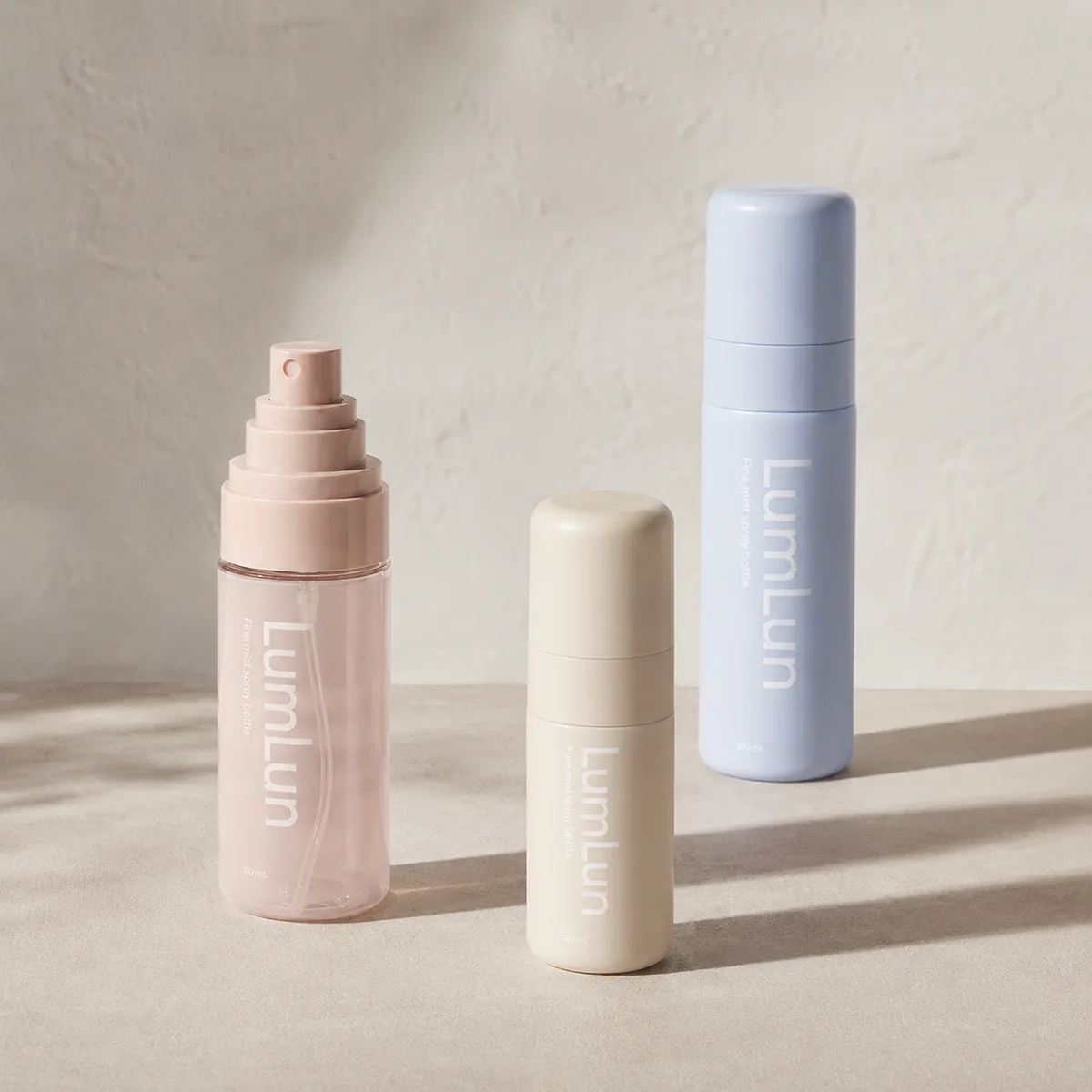Three Lumlun fine mist spray bottles with a pink open pump bottle and tall blue 100ml bottle.