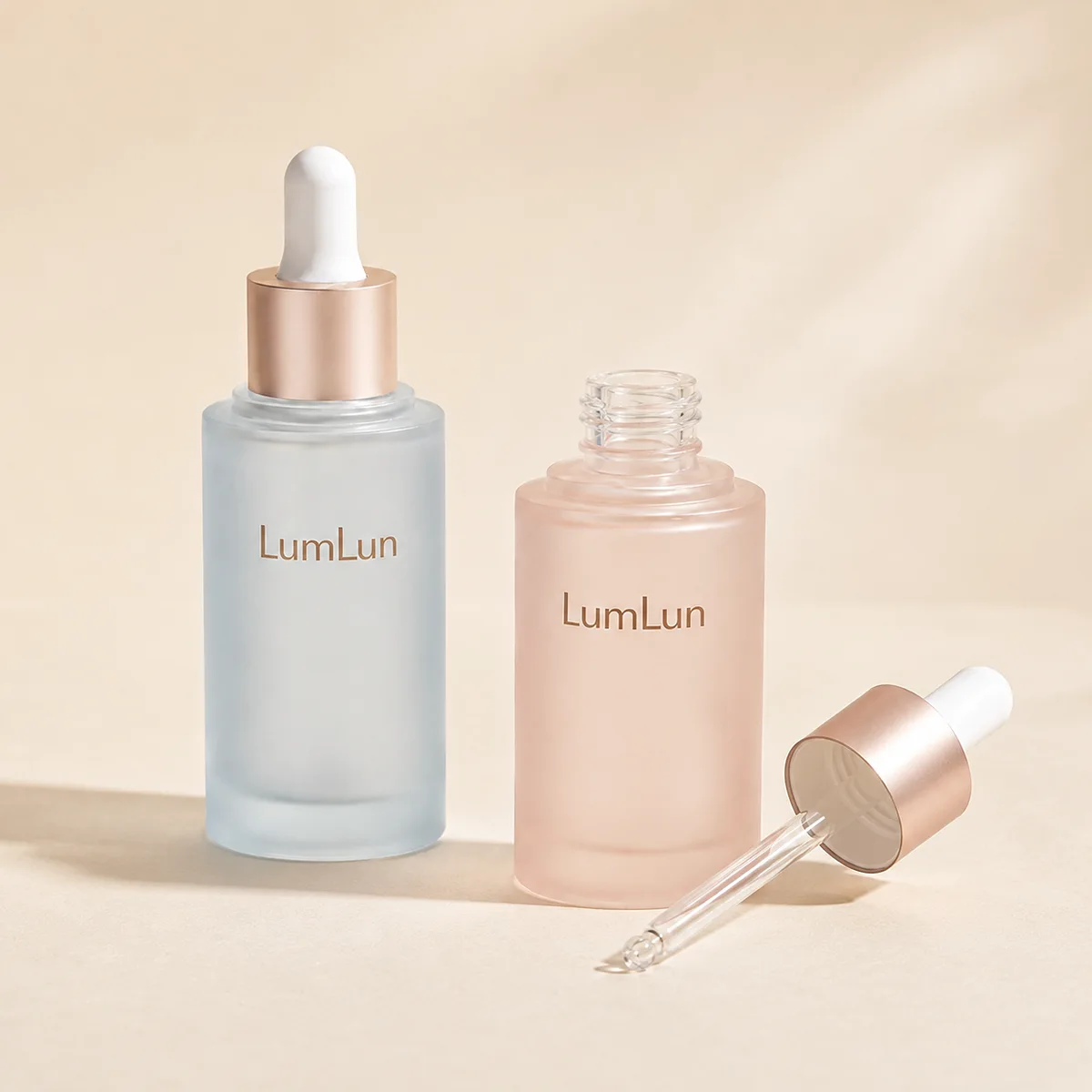 Lumlun flat shoulder PETG dropper bottles in blue and pink with one open glass pipette beside them.