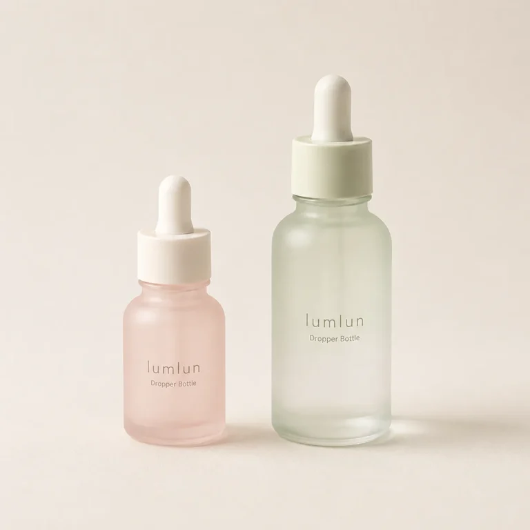 Two frosted glass dropper bottles in pastel colors shown slightly tilted together in a soft studio lighting setup.