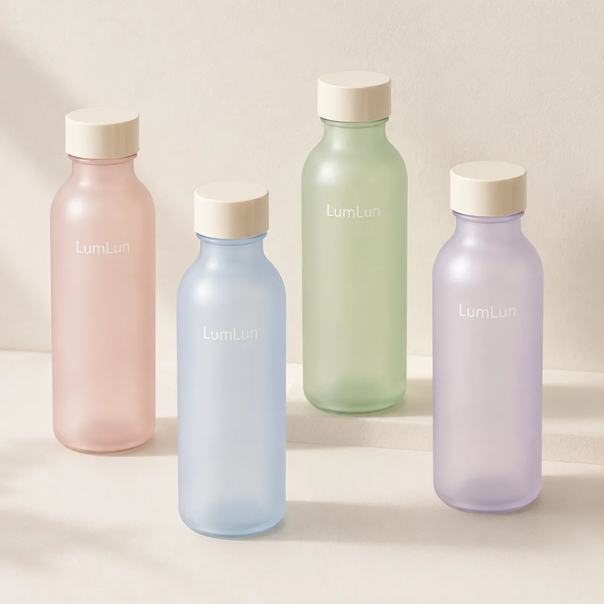 Four pastel glass toner bottles standing upright in balanced studio composition with soft neutral lighting