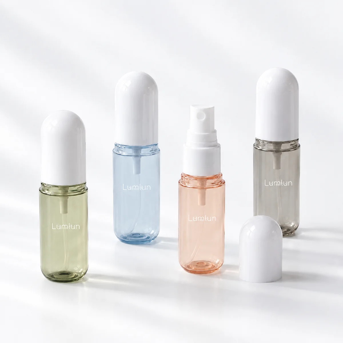 Four PET capsule fine mist spray bottles in sage, blue, peach and smoky grey, with one sprayer exposed