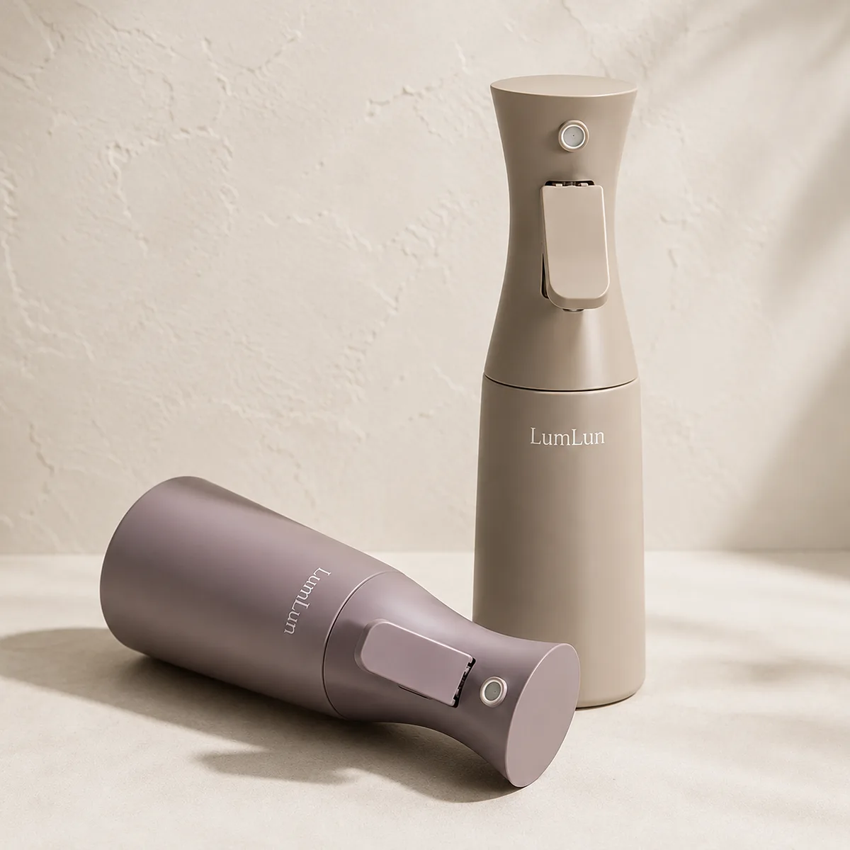 Lumlun PET continuous fine mist spray bottles in taupe and mauve, with one bottle lying horizontally.