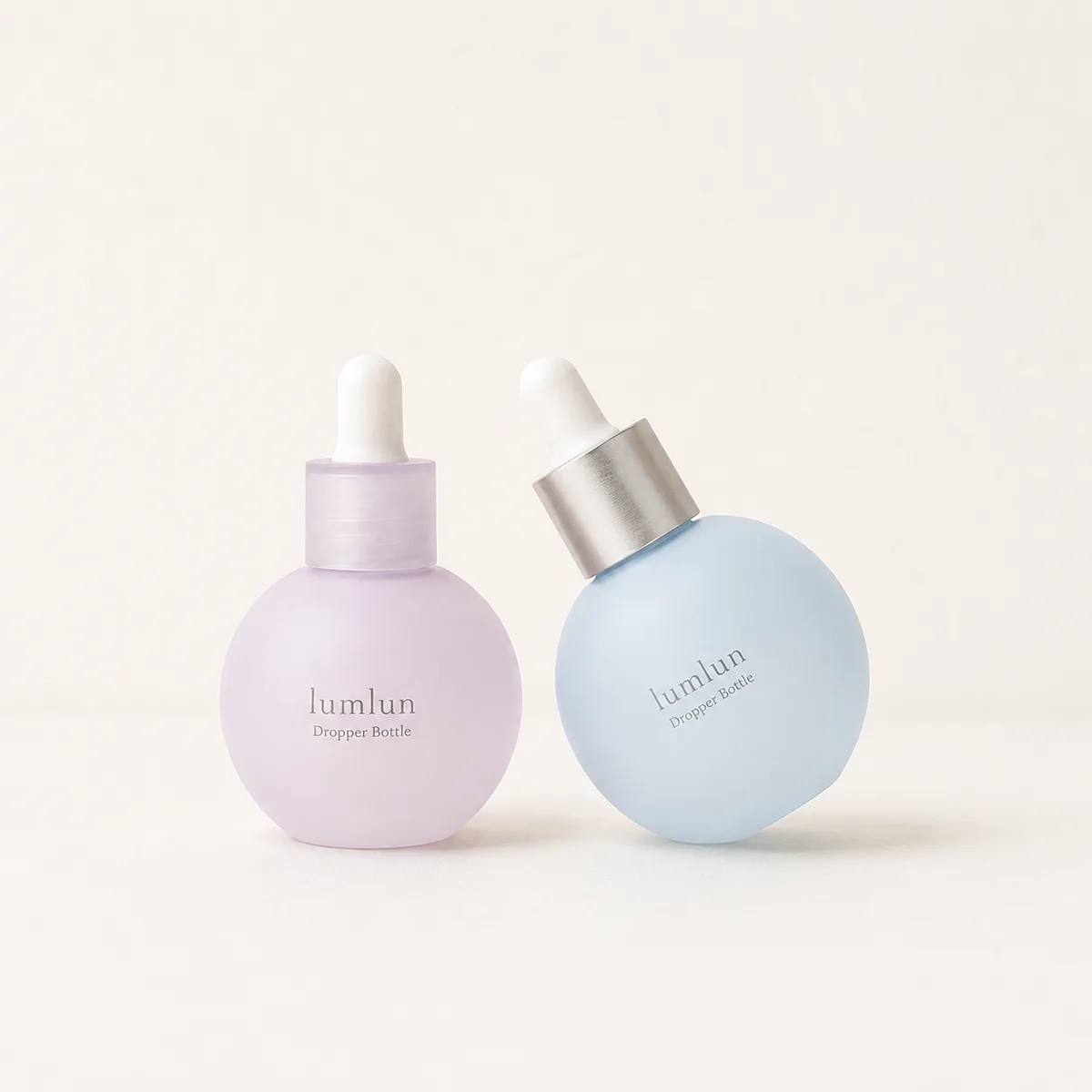 Two LumLun spherical glass dropper bottles in pastel purple and blue, one tilted for display.