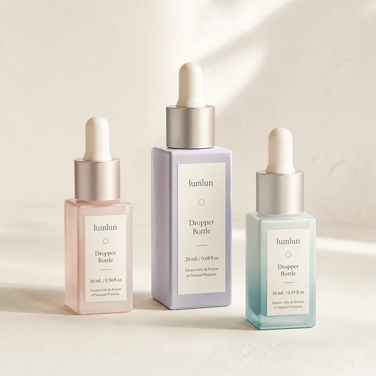 Three square glass dropper bottles with labeled front panels and silver caps in pink purple and teal arranged on a soft studio background.