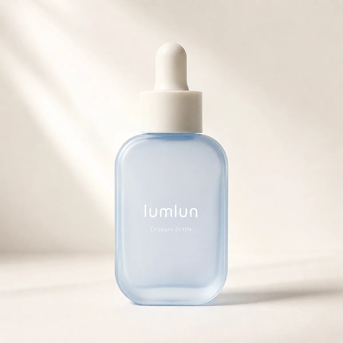 A single frosted square glass dropper bottle in soft blue displayed in a clean minimal studio setting.