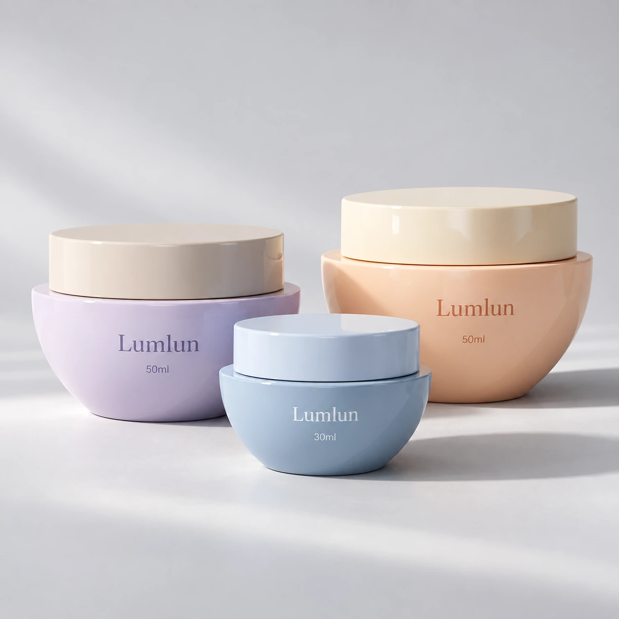 Tres tarros de crema LumLun de PP con forma de cuenco en azul, lila y melocotón, con tamaños de 30 y 50 ml