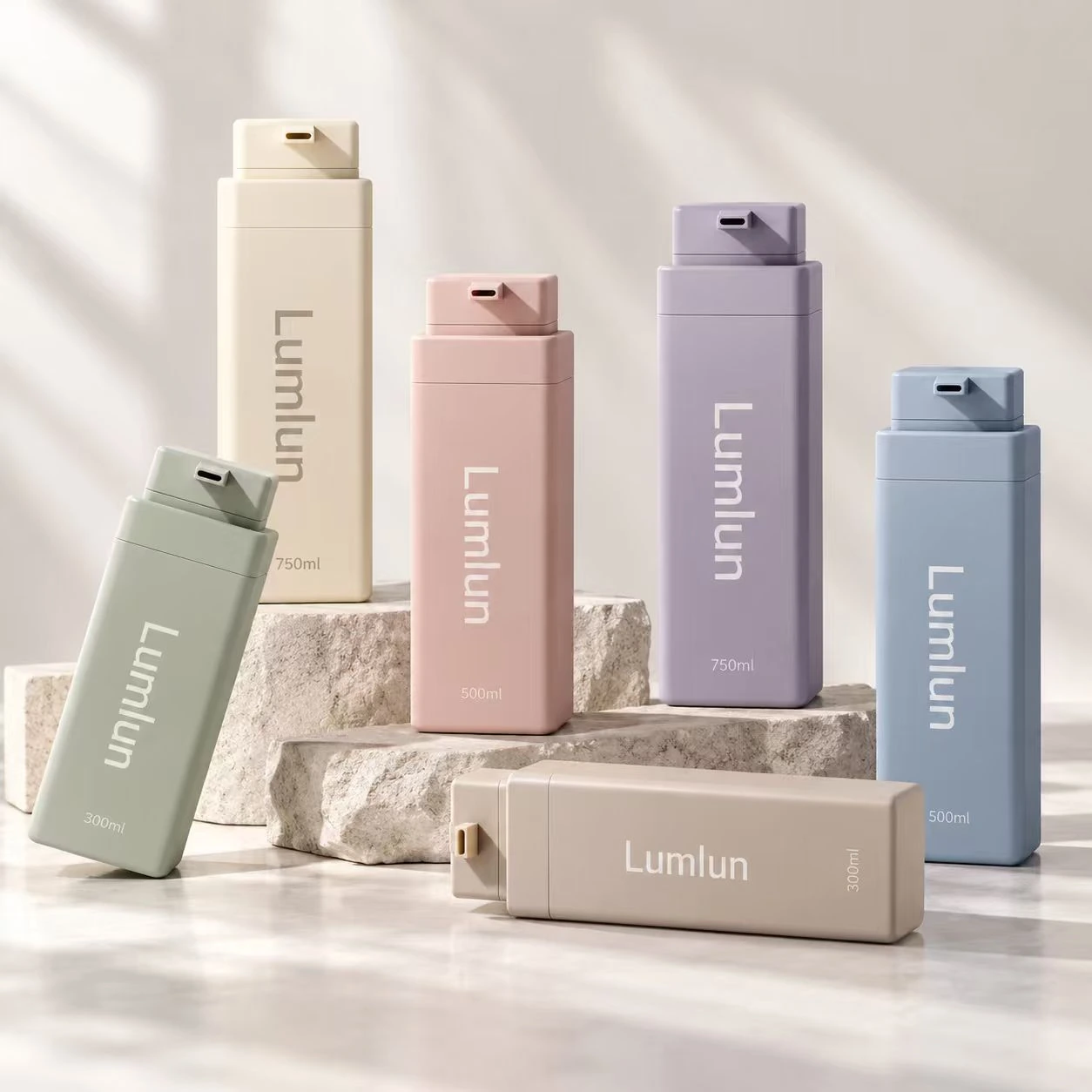 Varias botellas rectangulares PET grandes en colores pastel coordinados expuestas sobre bloques de piedra.