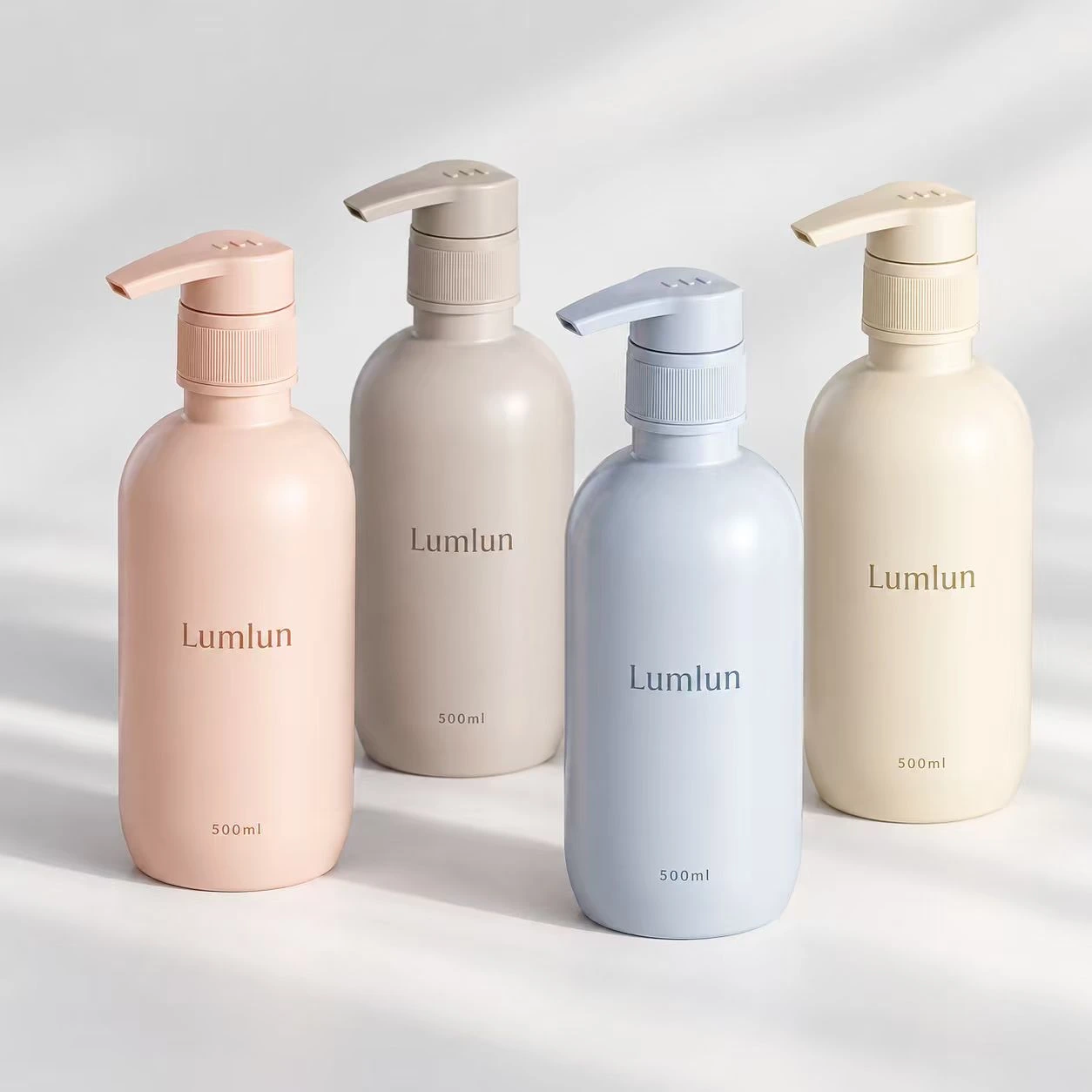 Vier abgerundete 500-ml-PET-Pumpflaschen in Pastellrosa, Taupe, Blau und Creme.